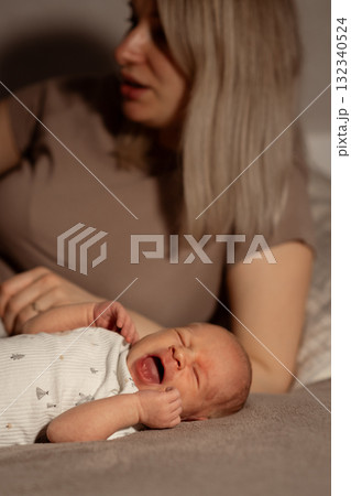 Mom comforts her crying baby while relaxing at home in a cozy setting during the evening hours Mom comforts her crying baby while relaxing at home in a cozy setting during the evening hours 132340524
