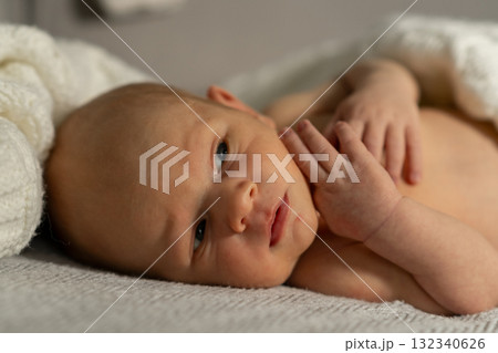 Baby lying on a soft blanket, gazing curiously while reaching out with a tiny hand during a calm indoor moment 132340626