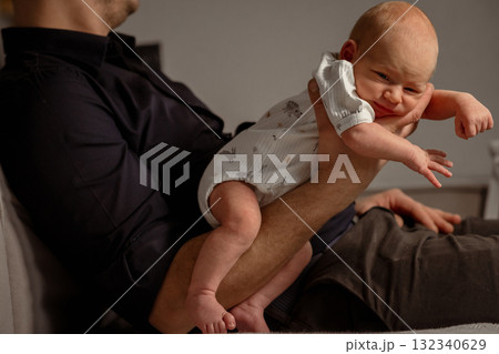 Baby happily playing on a parents leg while relaxing on a comfortable couch during a cozy indoor moment 132340629