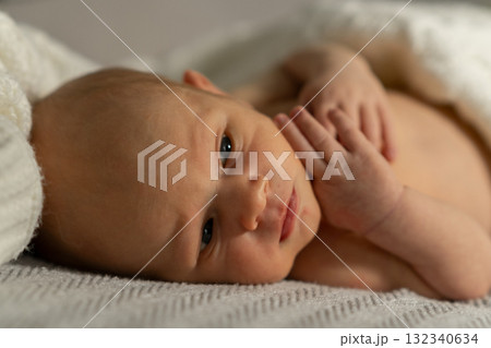 Sweet newborn baby lying on a cozy blanket with soft lighting, showcasing tiny hands and curious expression in a serene indoor setting Sweet newborn baby lying on a cozy blanket with soft lighting, showcasing tiny hands and curious expression in a serene indoor setting 132340634
