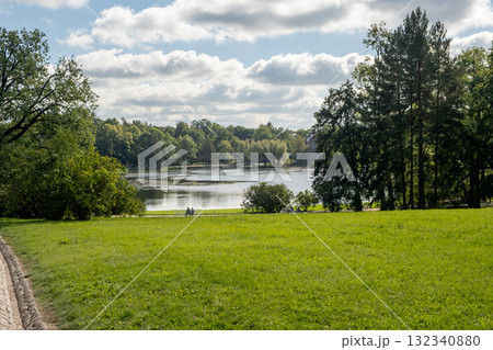 Scenic view of Catherine Palace grounds featuring serene lake and lush greenery on a clear day with visitors enjoying nature Scenic view of Catherine Palace grounds featuring serene lake and lush greenery on a clear day with visitors enjoying nature 132340880