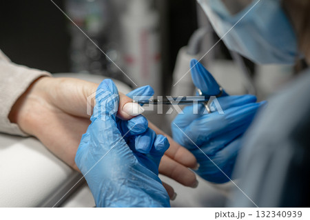 Nail technician performing manicure with precision in a well lit salon setting 132340939