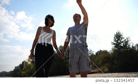 Romantic couple holding hands of each other and walking at coastline. Happy pair going along seashore at sunny day. Lovers spending time together at resort. Concept of vacation or holiday. Slow motion 132341457