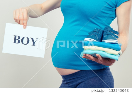 Woman in pregnant holding card with inscription boy and clothes for newborn 132343048