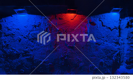 Rough plaster wall lit by blue and red spotlights, heavy texture and moody color creating dramatic abstract backdrop 132343580