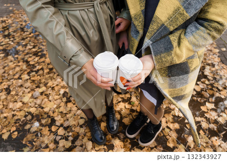 Autumn Coffee Date: Two People Holding Warm Drinks Outdoors, Fall Leaves, Beige Trench Coat, Plaid Scarf, Cozy Aesthetic, Lifestyle Photography. Autumn Coffee Date: Two People Holding Warm Drinks Outdoors, Fall Leaves, Beige Trench Coat, Plaid Scarf, Cozy Aesthetic, Lifestyle Photography. 132343927