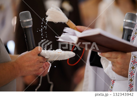Orthodox Christian Blessing Ceremony: Priest with Microphone, Feathers, Open Book, White Vestments, Spiritual Ritual, Religious Practice, Golden Details. Orthodox Christian Blessing Ceremony: Priest with Microphone, Feathers, Open Book, White Vestments, Spiritual Ritual, Religious Practice, Golden Details. 132343942