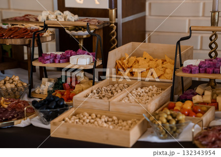 Gourmet Charcuterie Board Display with Variety of Cheeses, Meats, Nuts and Olives on Wooden Stands, Dark Background, Appetizer Table Setup. 132343954