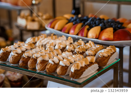 Elegant Dessert Spread with Cream Puffs, Fresh Fruit Platter, and Golden-Brown Pastries on Tiered Display, Luxurious Brown Tones. Elegant Dessert Spread with Cream Puffs, Fresh Fruit Platter, and Golden-Brown Pastries on Tiered Display, Luxurious Brown Tones. 132343959