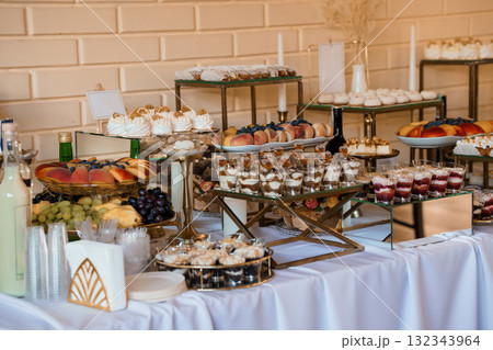 Elegant Dessert Buffet Display with Golden Stands, Fresh Fruit, Pastries and White Tablecloth Wedding Celebration, Gold Tones. 132343964