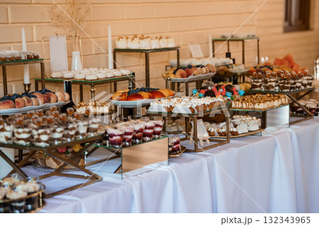 Luxurious Dessert Table Display at Wedding Reception with Gold Accents, White Linens, and Variety of Pastries. Luxurious Dessert Table Display at Wedding Reception with Gold Accents, White Linens, and Variety of Pastries. 132343965