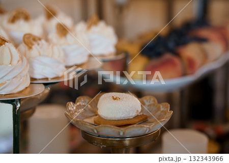 Elegant Dessert Display Featuring White Pavlovas with Gold Accents on Silver Platters, Wedding Cake Table, Soft Focus, Pastel Colors Elegant Dessert Display Featuring White Pavlovas with Gold Accents on Silver Platters, Wedding Cake Table, Soft Focus, Pastel Colors 132343966