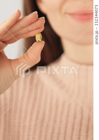 Close-up of an unrecognizable smiling woman holding a collagen capsule beauty supplement. Concept of skincare, anti aging, self care and daily wellness routine. 132344073