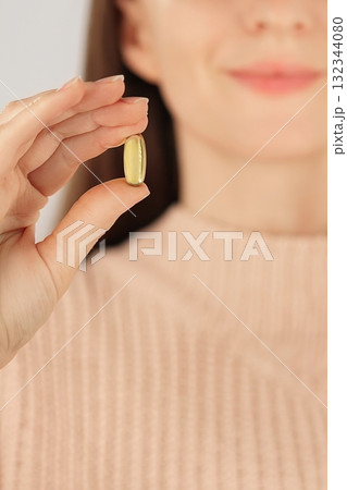 Vertical close-up of an unrecognizable woman hollding a fish oil capsule, promoting daily supplement and heart health.  132344080