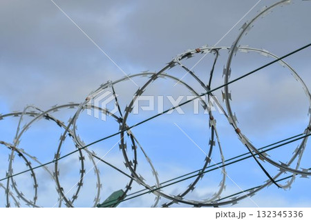 Barbed razor wire on a high-security building. Barbed wire and heavy wire fencing. Design of prisons, military facilities, nuclear power plants, and defense against illegal migration. Barbed razor wire on a high-security building. Barbed wire and heavy wire fencing. Design of prisons, military facilities, nuclear power plants, and defense against illegal migration. 132345336