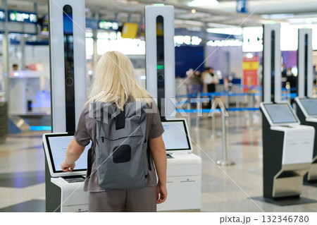 Woman checking in at an airport using self-service kiosk amid a busy terminal environment early in the morning 132346780