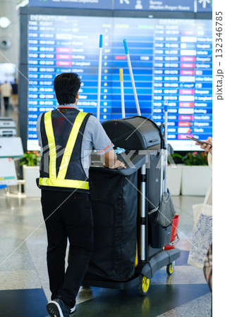 Airport staff member performs cleaning duties with a cart in busy terminal during afternoon hours as travelers move about Airport staff member performs cleaning duties with a cart in busy terminal during afternoon hours as travelers move about 132346785