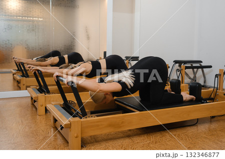 Group of women practicing pilates on reformers in a bright studio environment during a fitness class session in the afternoon Group of women practicing pilates on reformers in a bright studio environment during a fitness class session in the afternoon 132346877
