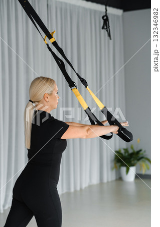 Woman using suspension straps for workout in a fitness studio during daylight focusing on strength training and body conditioning exercises 132346982