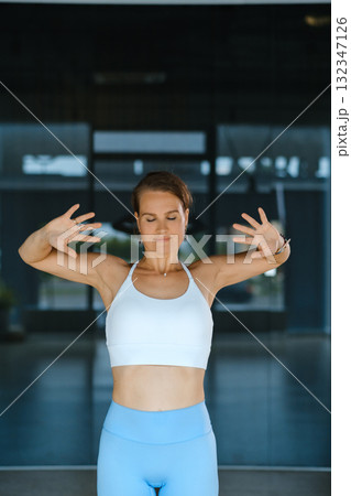 Woman practicing mindful breathing and stretching in a modern fitness studio during daytime to enhance relaxation and wellbeing 132347126