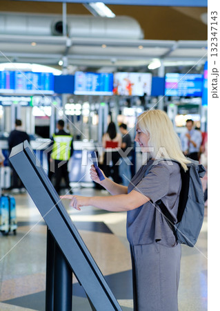 Traveler uses self-check-in kiosk at busy airport while preparing for upcoming flight to an international destination Traveler uses self-check-in kiosk at busy airport while preparing for upcoming flight to an international destination 132347143