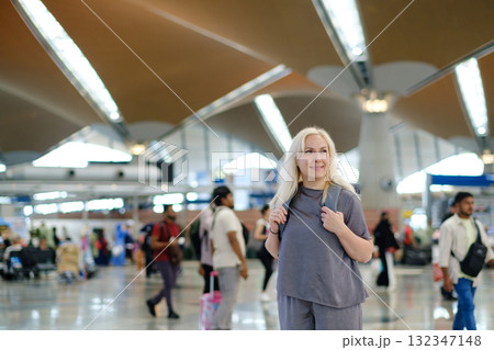 Woman standing in a busy international airport terminal with people walking around and modern architecture in the background during daytime travel hours 132347148
