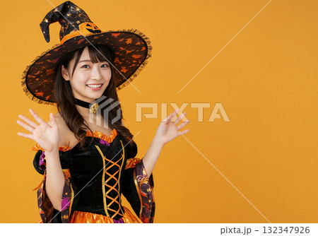 オレンジ背景に魔女の仮装をする女性 132347926