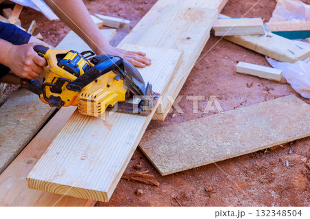 Carpenter expertly cuts long wooden planks with circular saw while working at construction site 132348504