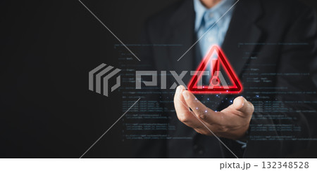 A businessman holds a glowing red warning triangle with an exclamation mark, symbolizing alert, caution, and cybersecurity threat in digital systems, with code elements in the background. 132348528