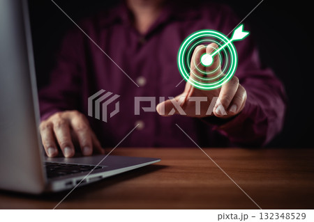person in shirt uses a laptop while digitally pressing a glowing green target icon with an arrow, symbolizing precision, achievement, success, goal setting, and business focus in technology. 132348529