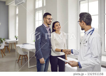 Professional obstetrician-gynecologist talks to happy family, shaking hands with smiling girl. 132351138