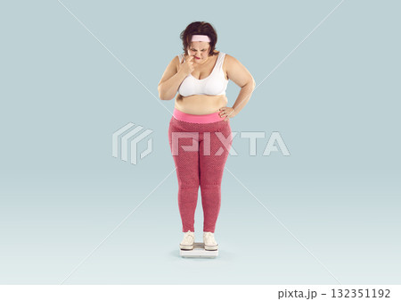 Overweight young woman weighs herself on scales and becomes worried about her weight 132351192