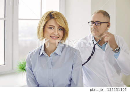 Mature patient in clinic for checkup. Doctor with stethoscope examining woman's lungs and heartbeat Mature patient in clinic for checkup. Doctor with stethoscope examining woman's lungs and heartbeat 132351195