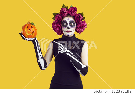 Amazed woman with creative Halloween face art with surprised expression showing decorative pumpkin. Amazed woman with creative Halloween face art with surprised expression showing decorative pumpkin. 132351198