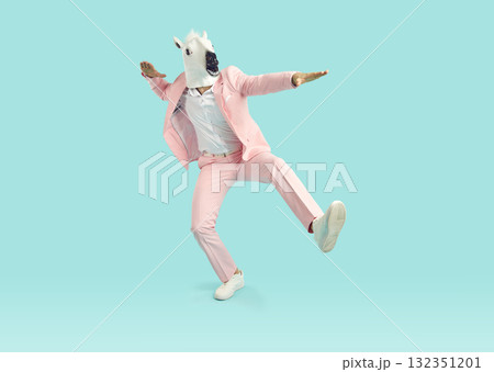 Funny man in horse mask and pink party suit dancing in studio with blue background 132351201