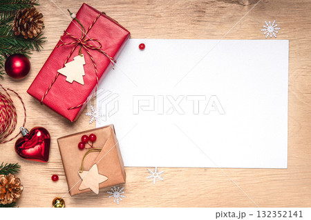 Christmas flat lay background: kraft wrapped gifts with wooden tags, twine and packing supplies on a wooden table. Blank white card for text. Ideal for greetings and New Year goals Christmas flat lay background: kraft wrapped gifts with wooden tags, twine and packing supplies on a wooden table. Blank white card for text. Ideal for greetings and New Year goals 132352141
