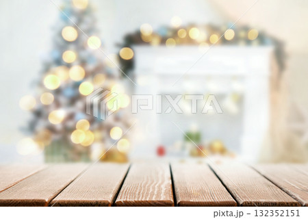 Warm holiday background: wooden tabletop in front, blurred room with fireplace, Christmas tree and golden lights. Cozy bokeh and ample copy space for banners, headers and greetings. 132352151