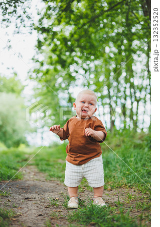 Little boy 1 year old takes his first steps outside. Child learns to walk. Summer football for babies. 132352520