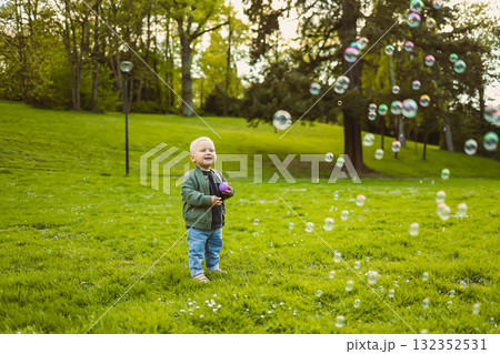 Little 2 year old boy running on green grass with soap bubbles. Toddler boy enjoying a walk in nature. Child having fun in city park. Little 2 year old boy running on green grass with soap bubbles. Toddler boy enjoying a walk in nature. Child having fun in city park. 132352531