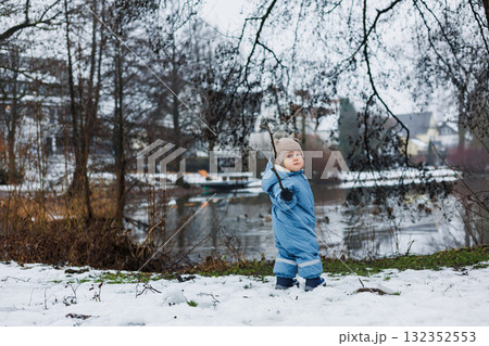 A joyful child is playing happily in a snowy winter landscape near the lake, surrounded by the picturesque beauty of nature and the serene qualities of the snowcovered environment A joyful child is playing happily in a snowy winter landscape near the lake, surrounded by the picturesque beauty of nature and the serene qualities of the snowcovered environment 132352553