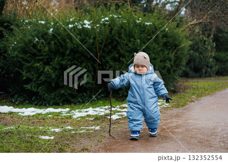 A child joyfully exploring nature in a warm winter outfit, holding a stick and smiling A child joyfully exploring nature in a warm winter outfit, holding a stick and smiling 132352554