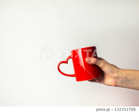 A hand holding a red cup with a heart shaped handle A hand holding a red cup with a heart shaped handle 132352709
