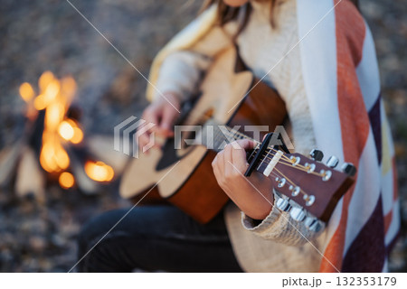 Young woman playing the guitar near the bonfire on campsite. Girl in warm striped plaid playing the guitar, sitting near bonfire in evening on nature Young woman playing the guitar near the bonfire on campsite. Girl in warm striped plaid playing the guitar, sitting near bonfire in evening on nature 132353179