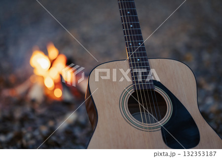 Close-up shot of acoustic guitar near bonfire outdoors. New guitar standing near burning campfire in the evening, spending time outdoors on nature 132353187