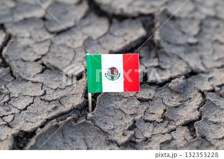 Flag of Mexico on dry cracked soil. Concept of drought in Mexico, rainless season, lack of water 132353228