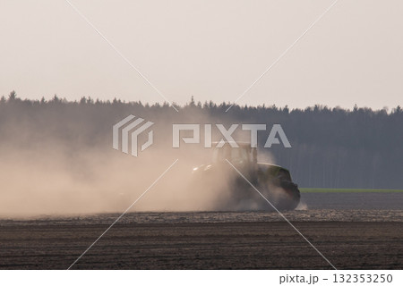 Tractor plowing farm land in spring. Tractor working on field, cultivating ground, dust covering rear part of tractor, plowing field for growing some grain or vegetables Tractor plowing farm land in spring. Tractor working on field, cultivating ground, dust covering rear part of tractor, plowing field for growing some grain or vegetables 132353250
