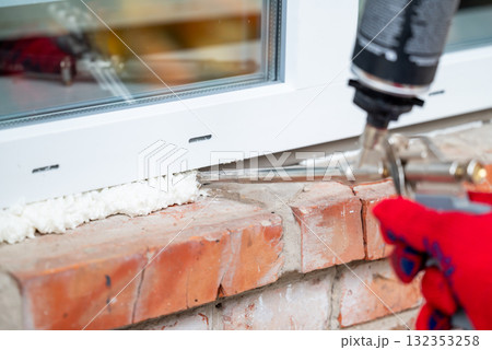 Installing new modern window. Hand of a worker foams stitches around installed window with a foam gun 132353258