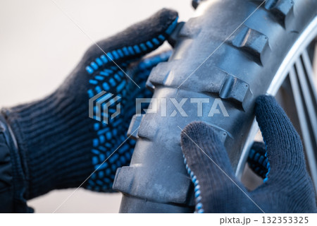 Technician mechanic looking through worn out tire of motorcycle. Tire needs replacement, dangerous to drive on bald tire Technician mechanic looking through worn out tire of motorcycle. Tire needs replacement, dangerous to drive on bald tire 132353325