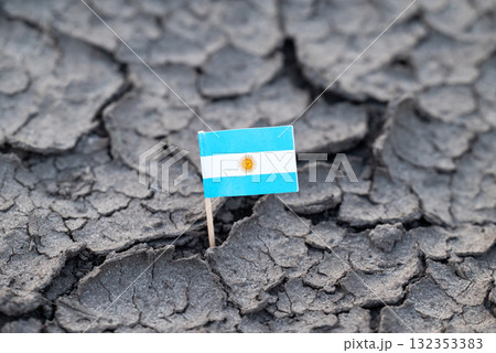 Argentine flag in arid, cracked soil. A small flag of Argentina stuck in cracked dry earth, symbolizing environmental degradation and national challenges 132353383