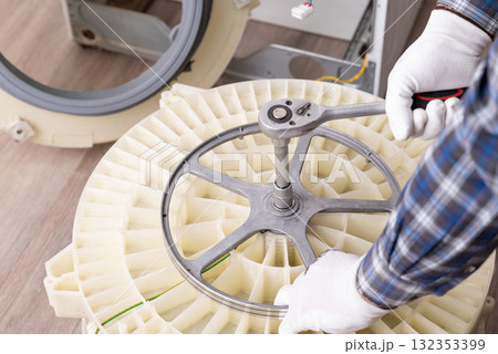 Repairing a washing machine with tools in a service workshop. A technician uses a wrench to fix a washing machine in a service workshop, focusing on the drum assembly Repairing a washing machine with tools in a service workshop. A technician uses a wrench to fix a washing machine in a service workshop, focusing on the drum assembly 132353399